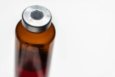 Kehribar rengi aşı enjeksiyon şişesinin seçici odak noktası beyaz arka planda olan bir makro çekim..