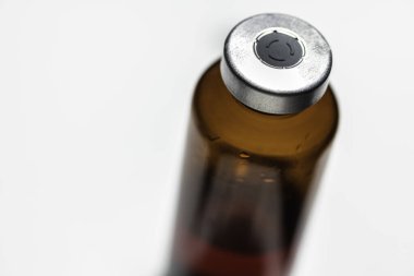 Kehribar rengi aşı enjeksiyon şişesinin seçici odak noktası beyaz arka planda olan bir makro çekim..