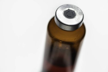 Kehribar rengi aşı enjeksiyon şişesinin seçici odak noktası beyaz arka planda olan bir makro çekim..