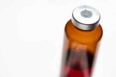 Kehribar rengi aşı enjeksiyon şişesinin seçici odak noktası beyaz arka planda olan bir makro çekim..