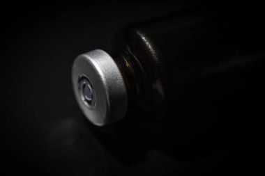 Kehribar rengi aşı enjeksiyon şişesinin seçici odak noktası olan bir makro çekim. Sade siyah zemin üzerine kurulmuş..