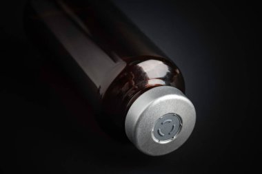 Kehribar rengi aşı enjeksiyon şişesinin özenli odak noktası dramatik siyah arkaplan üzerine kurulmuş bir makro çekim..