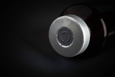 Kehribar rengi aşı enjeksiyon şişesinin özenli odak noktası dramatik siyah arkaplan üzerine kurulmuş bir makro çekim..