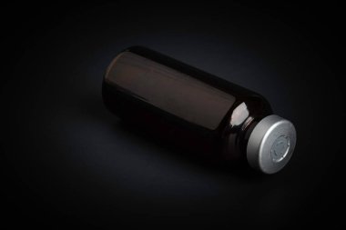 Kehribar rengi aşı enjeksiyon şişesinin özenli odak noktası dramatik siyah arkaplan üzerine kurulmuş bir makro çekim..