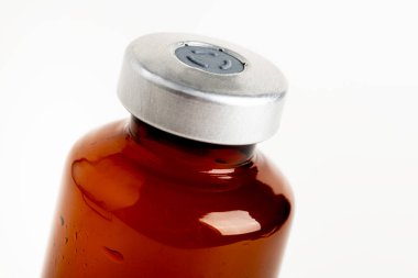 Kehribar rengi aşı enjeksiyon şişesinin seçici odak noktası beyaz arka planda olan makro bir çekim..