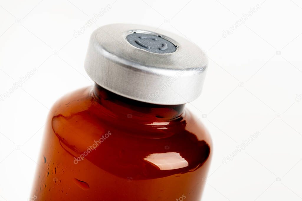 A macro shot with selective focus of an amber color vaccine injection bottle set on a plain white background.