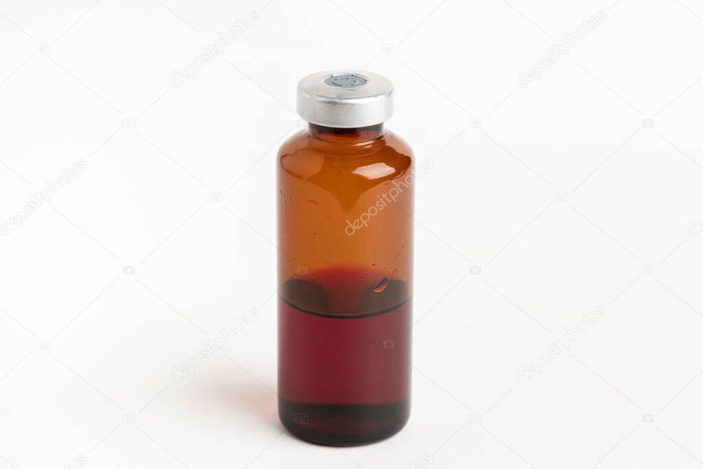 A macro shot with selective focus of an amber color vaccine injection bottle set on a plain white background.