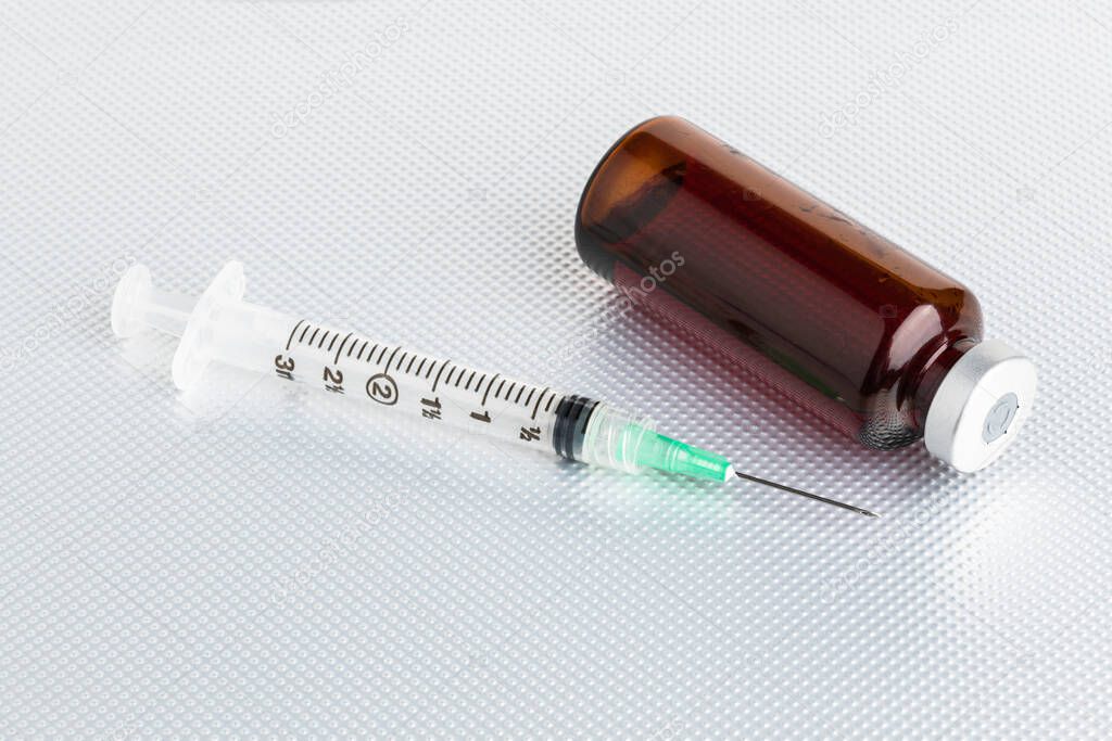 A close-up shot of an hygienic single-use plastic disposable medicine injection with amber color vial set on plain metal background.