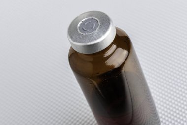 A macro shot with selective focus of an amber color vaccine injection bottle set on a metal background. clipart