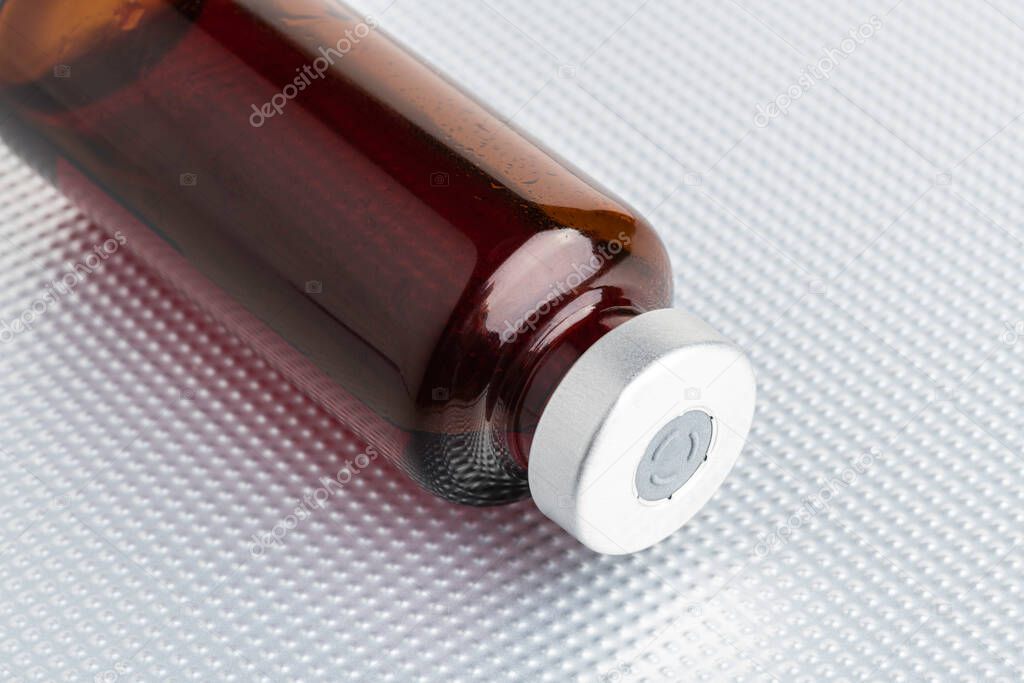 A macro shot with selective focus of an amber color vaccine injection bottle set on a metal background.
