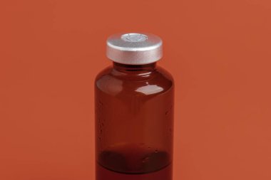 Kehribar rengi aşı enjeksiyon şişesinin seçici odak noktası olan kırmızı zemin üzerine kurulmuş bir makro çekim..