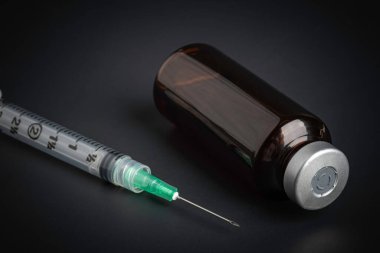 A close-up shot of an hygienic single-use plastic disposable syringe injection with amber color vial set on black background. clipart