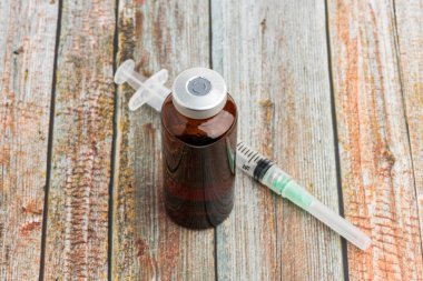 A close-up shot of an hygienic single-use plastic disposable syringe injection with amber color vial set on wood background. clipart