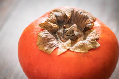 A macro shot with selective focus of a ripe persimmon fruit set on a wood table. clipart