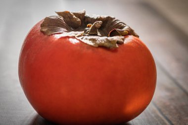 A macro shot with selective focus of a ripe persimmon fruit set on a wood table. clipart