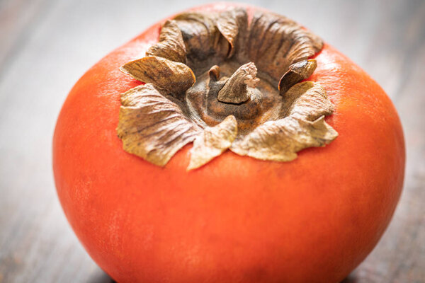 A macro shot with selective focus of a ripe persimmon fruit set on a wood table.