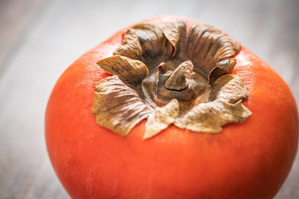 A macro shot with selective focus of a ripe persimmon fruit set on a wood table.