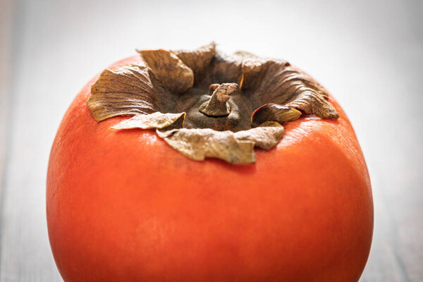 A macro shot with selective focus of a ripe persimmon fruit set on a wood table.