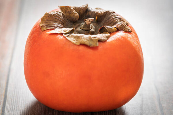 A macro shot with selective focus of a ripe persimmon fruit set on a wood table.