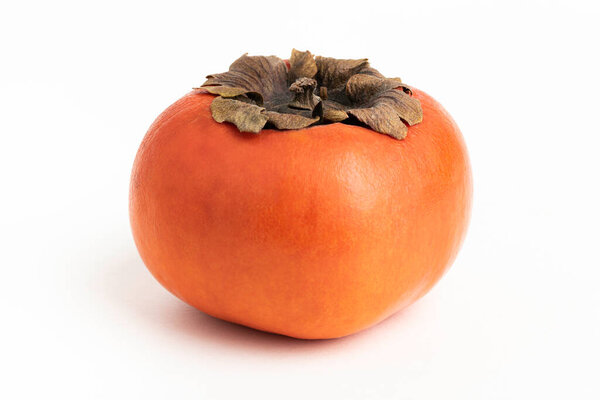 Close-up shot with shallow depth of field of a ripe persimmon fruit set on a plain white background.