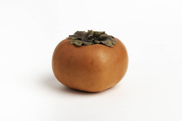Close-up shot with shallow depth of field of a ripe persimmon fruit set on a plain white background.