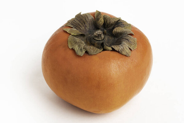 Close-up shot with shallow depth of field of a ripe persimmon fruit set on a plain white background.