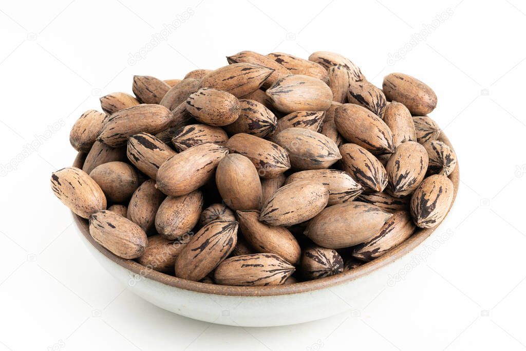 In-shell pecan nuts on bowl set on plain white background.