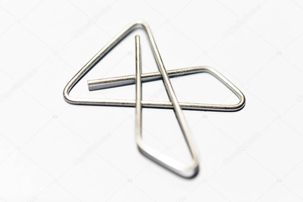 An extreme macro shot with selective focus of an x-style silver metal paper clip set on white background.