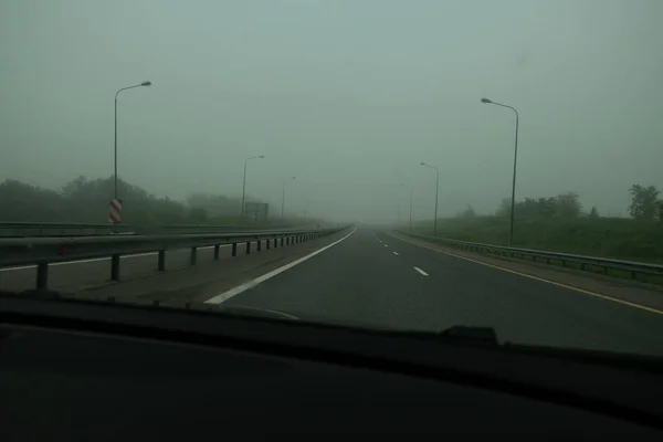 霧の中でアスファルト高速道路 車のフロントガラスを介して道路のビュー 車のない高速トラック 濃霧は視認性を制限する — ストック写真