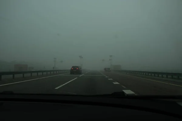 霧の中でアスファルト高速道路 車のフロントガラスを介して道路のビュー 車のない高速トラック 濃霧は視認性を制限する — ストック写真