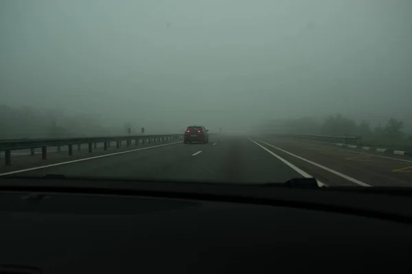 霧の中でアスファルト高速道路 車のフロントガラスを介して道路のビュー 車のない高速トラック 濃霧は視認性を制限する — ストック写真