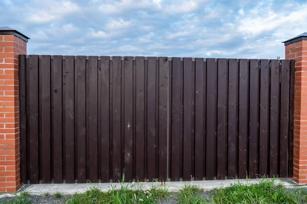 Wooden fence made of planed boards, picket fence. Fencing of a house, structure. Wooden gate. Territory protection. Day. Autumn. Russia.