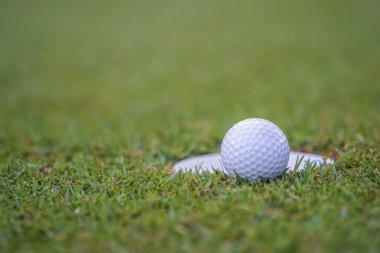 Golf sahasındaki delikte bir top. Golf topu golf sahasında kazanmak için golf sahasının yanındaki çimlere vuruyor.. 