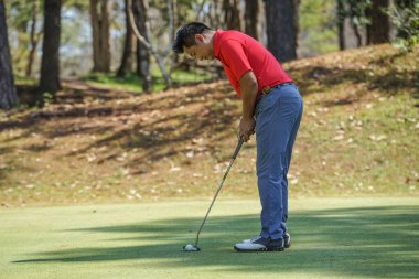Golfçü topu yeşil golfün üstüne koyuyor, mercek akşam vakti parlıyor. Golfçü vuruşu uzun süre deliğe soktuktan sonra kazanır..                               