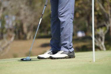 Golfçü topu yeşil golfün üstüne koyuyor, mercek akşam vakti parlıyor. Golfçü vuruşu uzun süre deliğe soktuktan sonra kazanır..                               