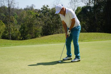 Golfçü topu yeşil golfün üstüne koyuyor, mercek akşam vakti parlıyor. Golfçü vuruşu uzun süre deliğe soktuktan sonra kazanır..                               