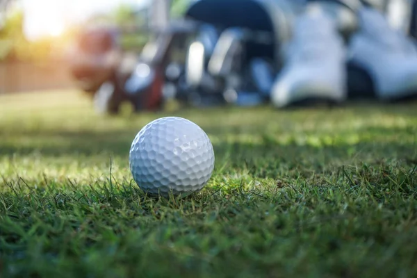 Closeup golf ball on green ready to be shot. Golf ball on green in the evening golf course with sunshine. Blurred set of golf clubs over green field background.