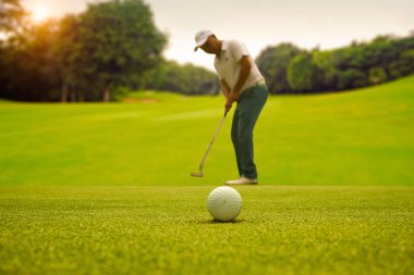 Siluet erkek golfçü golf topunu yeşil golfün üzerine koyuyor, güneş batarken mercek parlıyor..                               