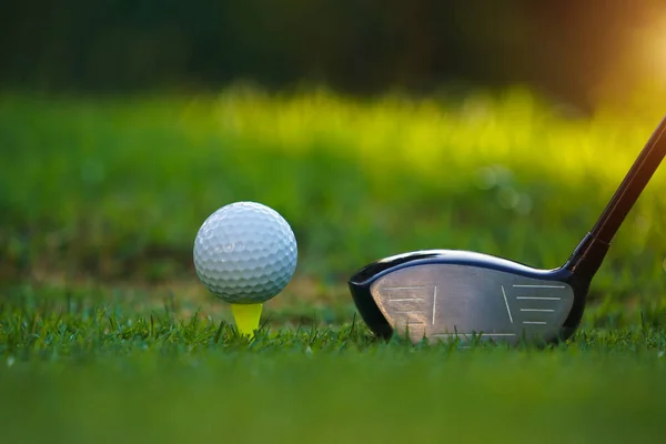 Golf club and golf ball on tee close up in grass field with morning sunshine. Ready for golf in the first short.