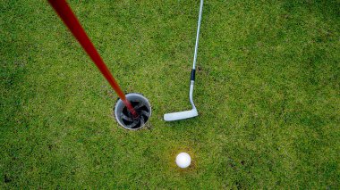 Golf topu yeşil çimlerin üzerinde sabah güneşli güzel bir golf sahasında. Golf topu, bayrak direğiyle deliğin yanındaki golf sahasında..                                