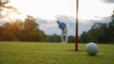 Golf topu yeşil çimlerin üzerinde sabah güneşli güzel bir golf sahasında. Golf topu, bayrak direğiyle deliğin yanındaki golf sahasında..                                