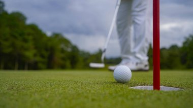 Golf topu yeşil çimlerin üzerinde sabah güneşli güzel bir golf sahasında. Golf topu, bayrak direğiyle deliğin yanındaki golf sahasında..                                
