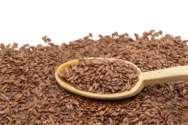 Üstünde kaşık olan keten tohumu ya da keten tohumu yığını beyaz arkaplan ile yukarıdan eğik görünüyor. 