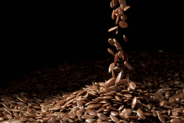 Close up of linseeds or flax seed on dark background with some falling in a narrow stream spread in the middle of the frame