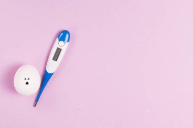 Pembe arka plan fotokopi alanı üzerinde termometresi olan üzgün bir yüzü olan Paskalya beyaz yumurtası. Paskalya 2021