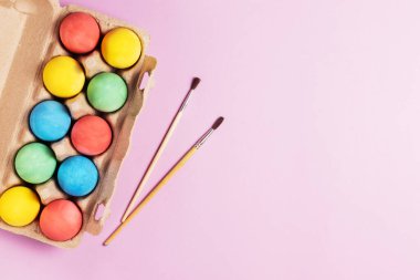 Ahşap bir tepside boyalı Paskalya yumurtaları ve pembe arka plan fotokopi alanında boya fırçaları.