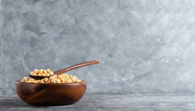 Tahta bir çevre dostu tabakta çiğ protein nohutları ve gri arka planda bir kaşık fotokopi alanı