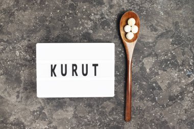 Geleneksel Asyalı kuru füme peyniri ahşap bir çevre dostu kaşığıyla siyah bir arka planda beyaz tahtaya kazınmış kurut yazısıyla birlikte.