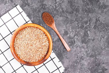 Bir sürü çiğ karabuğday, ahşap bir eko dostane tabakta, beyaz bir peçetede, kafeinsiz granüller dolusu karabuğday çayı ve gri arka plan fotokopi alanı.