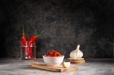 Tahtada beyaz bir tabakta Harissa acı sosu ve cam bir kavanozda sarımsak ve kırmızı biber.